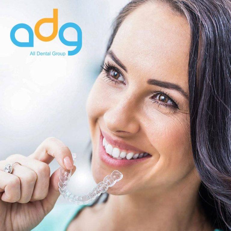 Smiling woman holding a clear aligner after treating dental issues with Invisalign