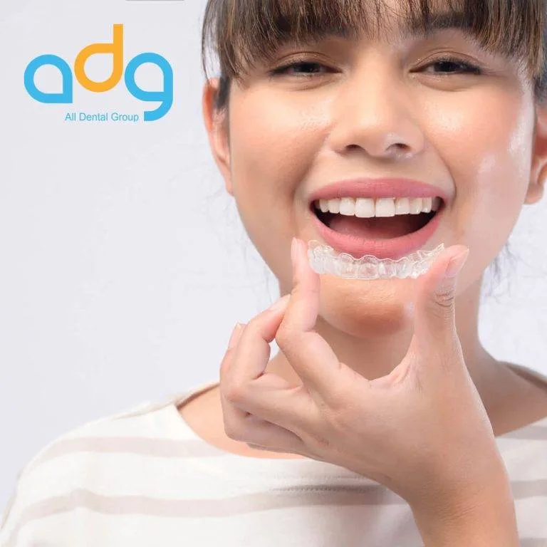 Smiling woman holding a clear aligner — Invisalign and teeth grinding